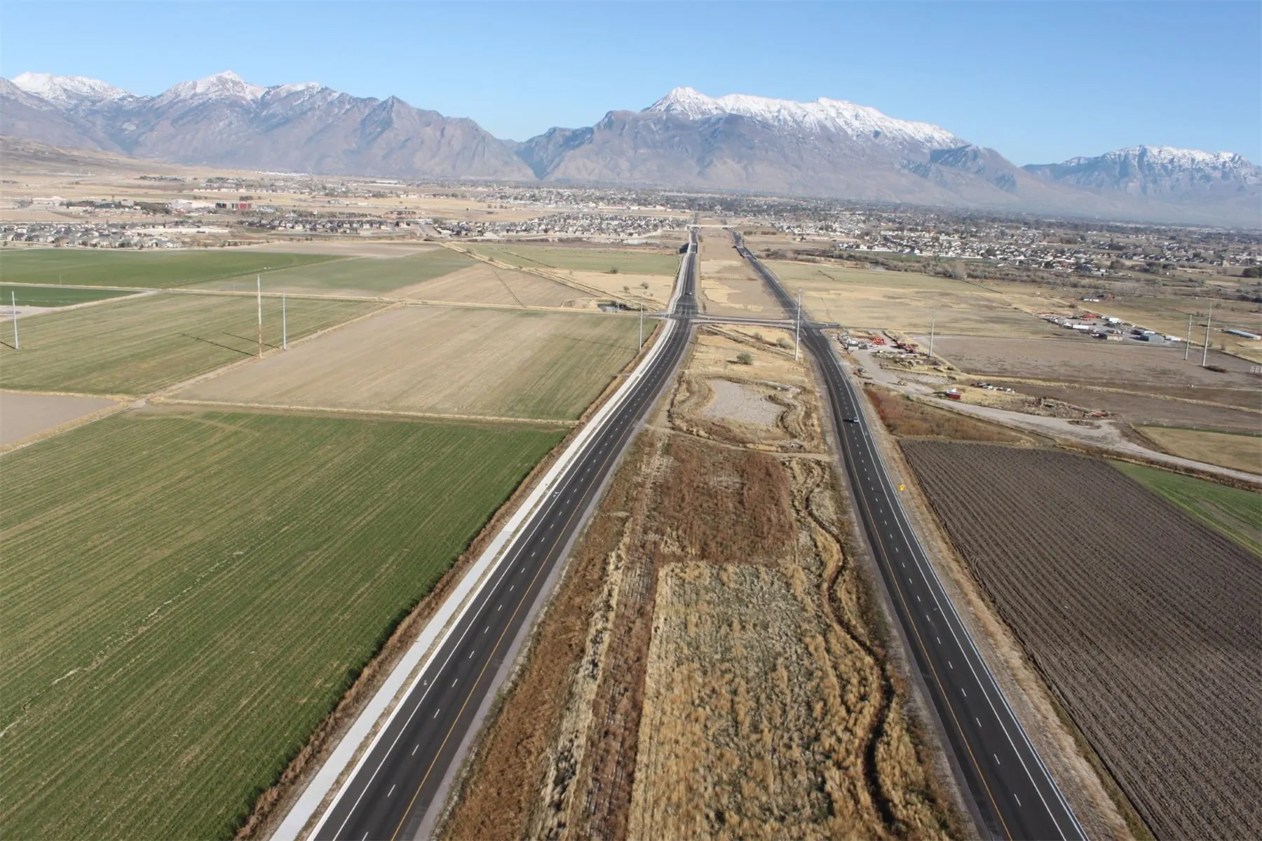 A divided highway running through farmland toward snow-capped mountains