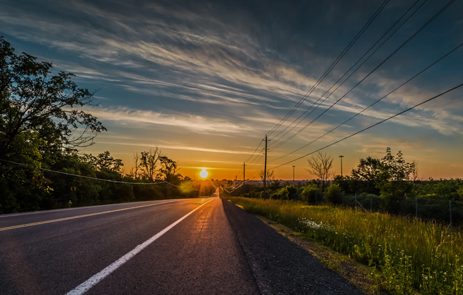 An empty road lined with power lines at sunset